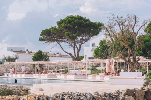 Swimming pool area with white buildings and trees at Experimental Group's Menorca hotel