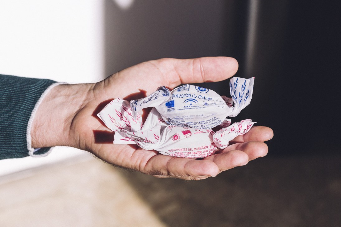 Hand holding individually wrapped polvorones de Estepa biscuits with blue and red printed wrappers.