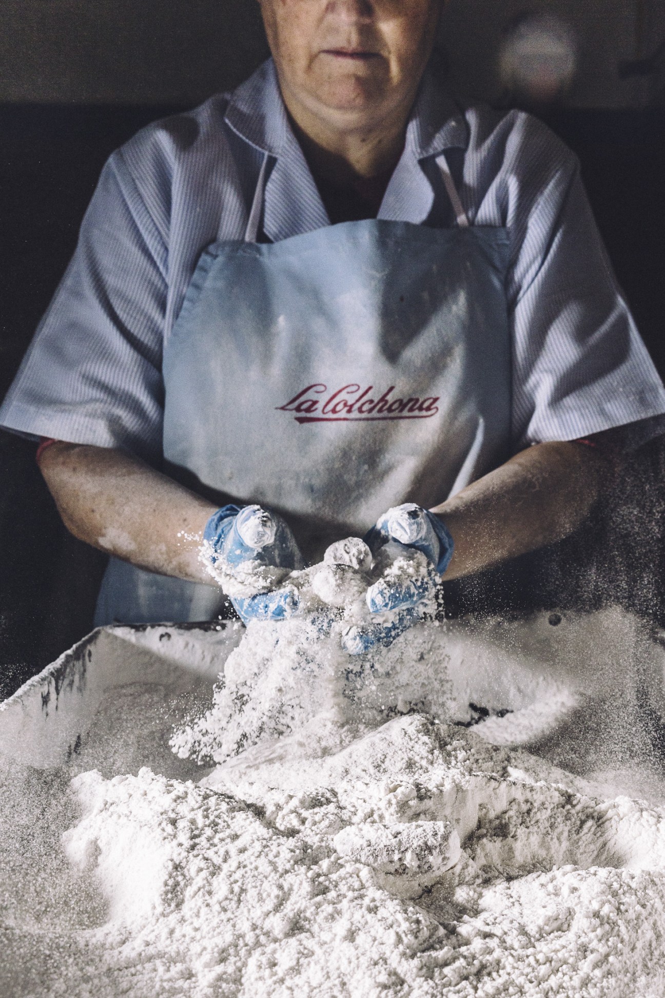 Worker at La Colchona factory coating hands in white powdered sugar while processing biscuits.