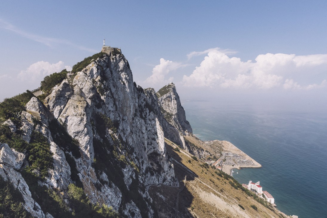 The distinctive white limestone Rock of Gibraltar rises dramatically from the coastline with a lighthouse at its peak and the Mediterranean Sea beyond.