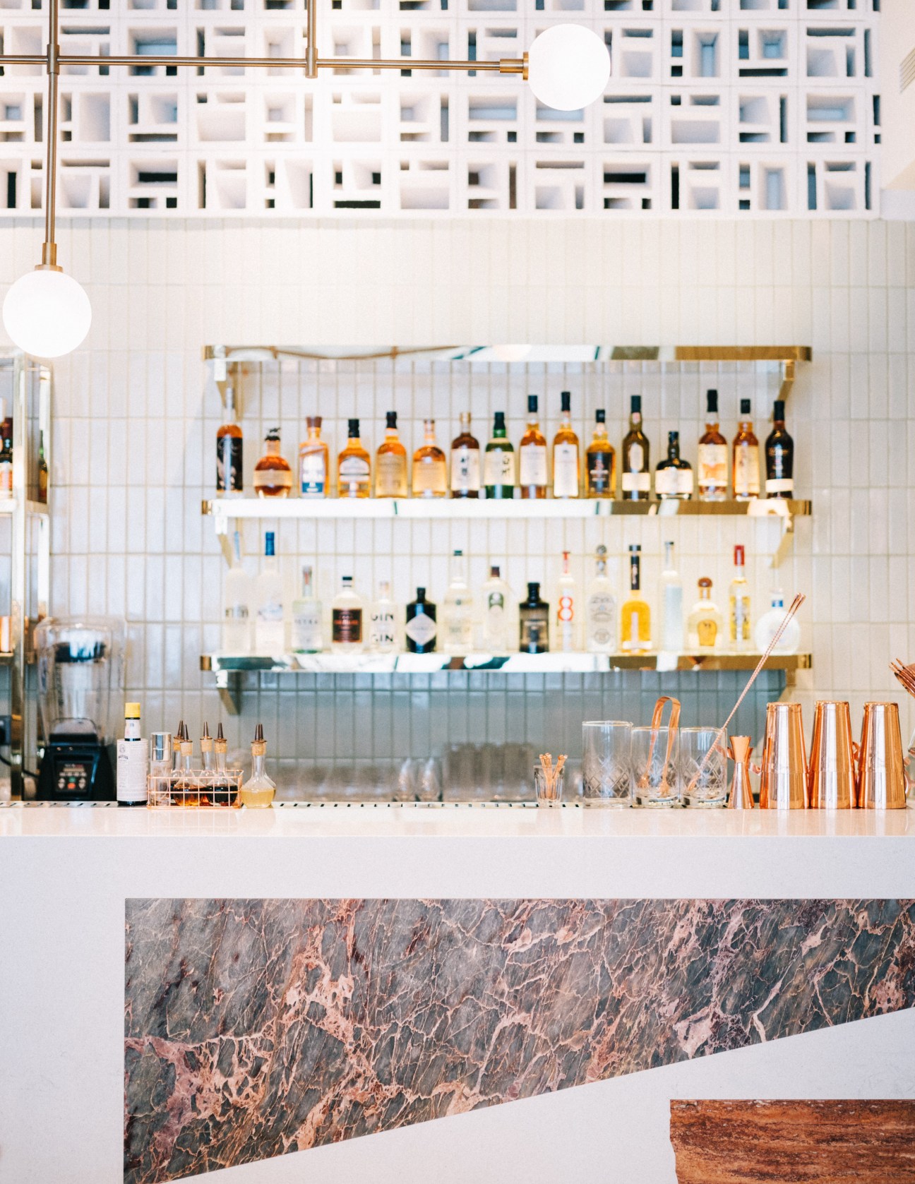 Well-stocked bar at Straits Clan with shelves of spirits, white subway tiles, brass fixtures and globe pendant lighting.