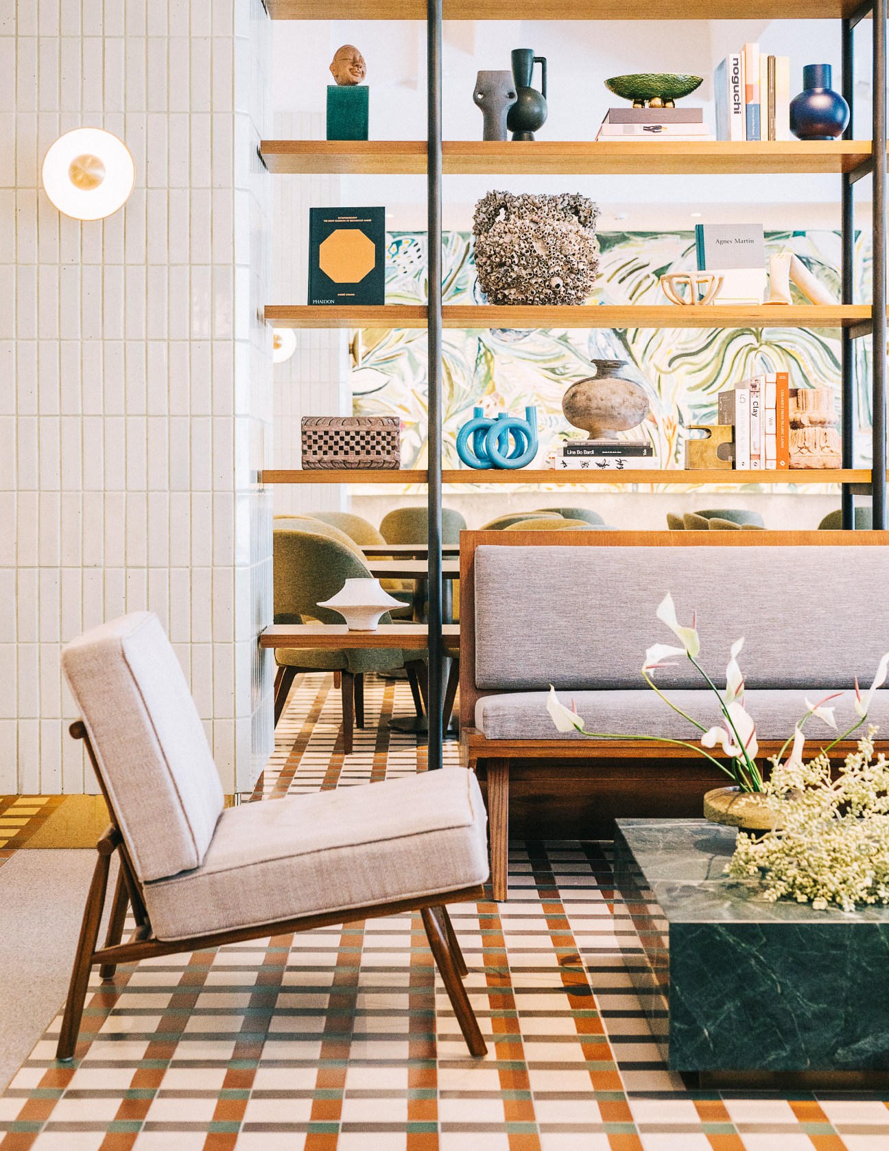 Interior seating area with mid-century chair, patterned floor tiles, wooden shelving with decorative objects and books at Straits Clan.
