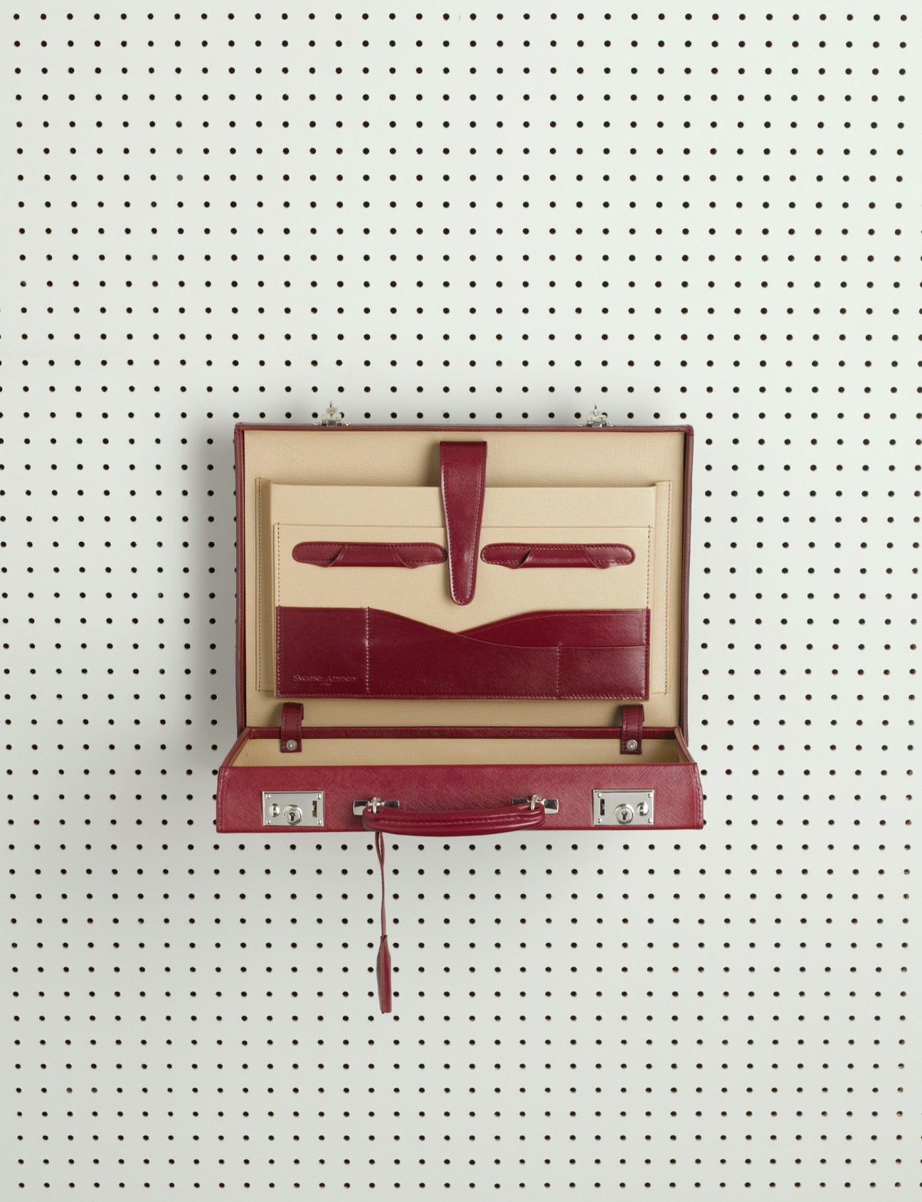 Burgundy leather briefcase with cream interior displayed open against pegboard background.