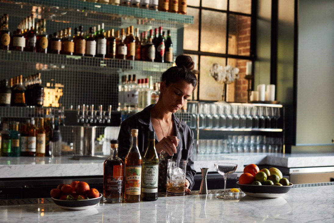 Bartender mixing cocktails at Firehouse Hotel bar with bottles on shelves behind.