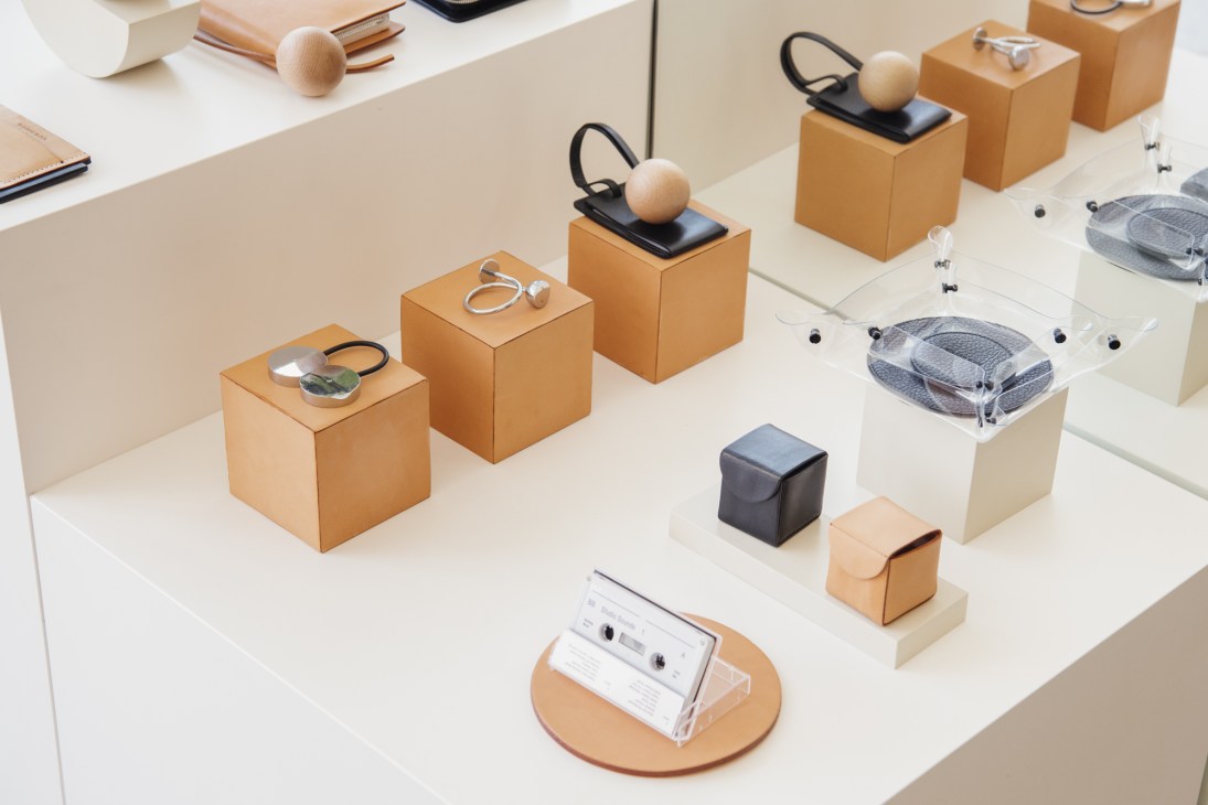 Building Block accessories displayed on white pedestals including leather bags, shoes, and geometric accessories.