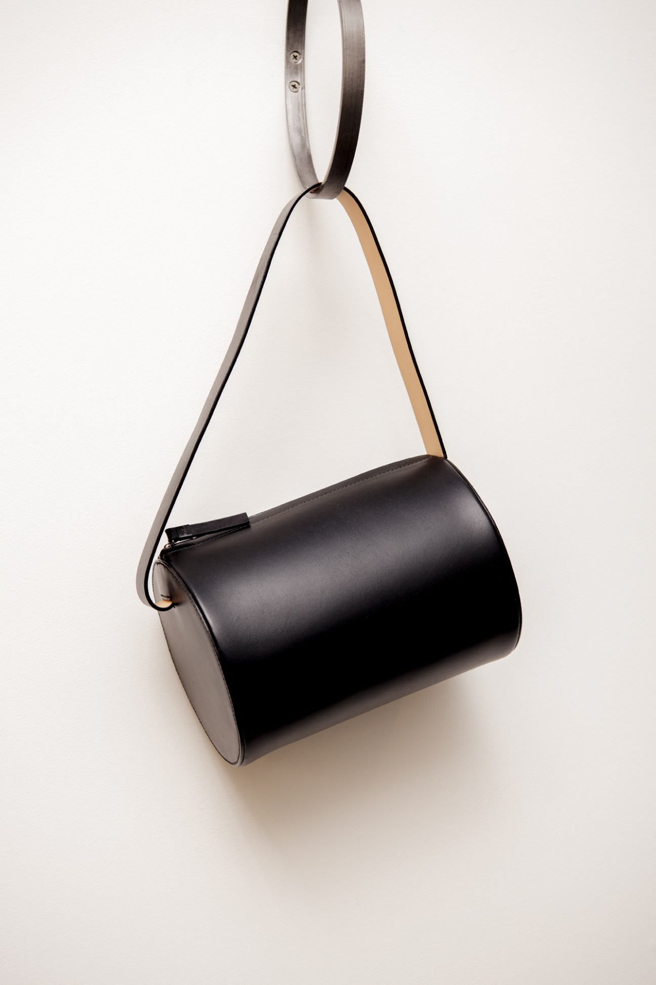Black cylindrical leather handbag with geometric design and gray fabric shoulder strap.
