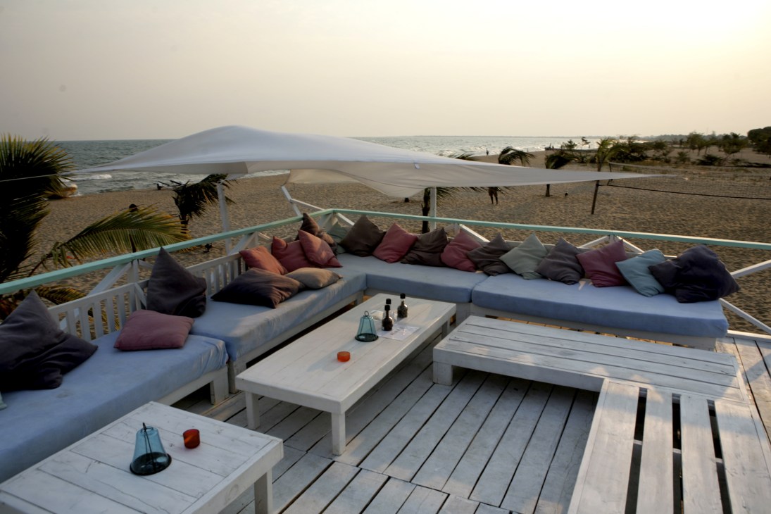 Bora Bora restaurant terrace on Lake Tanganyika with white loungers, colorful pillows and shaded seating overlooking the beach.