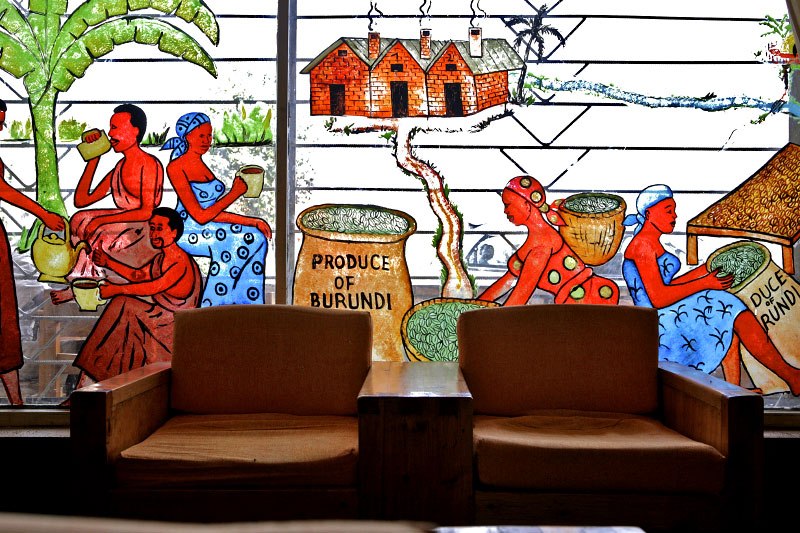 Two brown leather armchairs face a colorful mural depicting Burundi agricultural production and rural life.