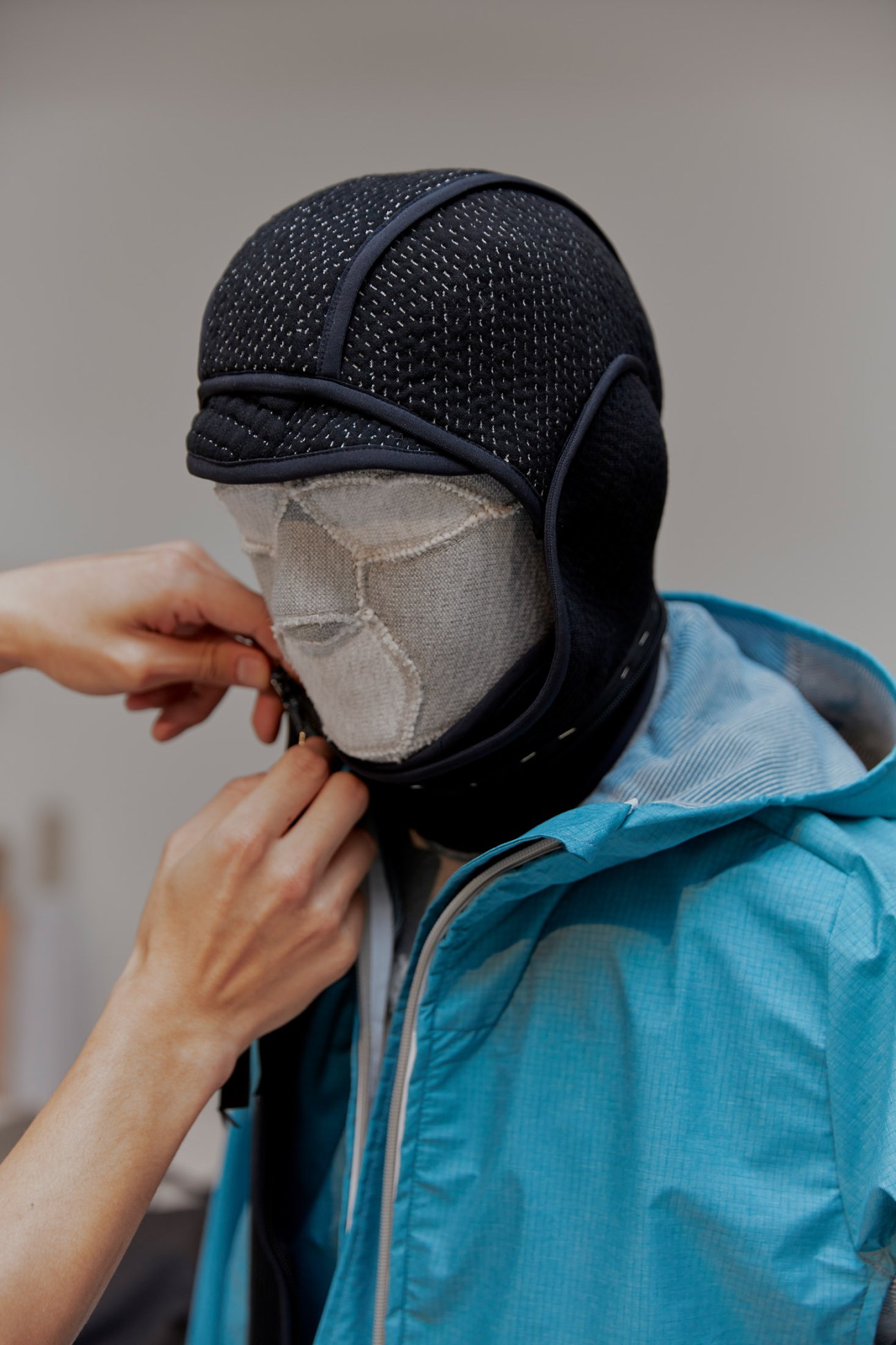 Black knitted headwarmer with mesh texture and gray fabric lining worn by a person in a blue jacket.