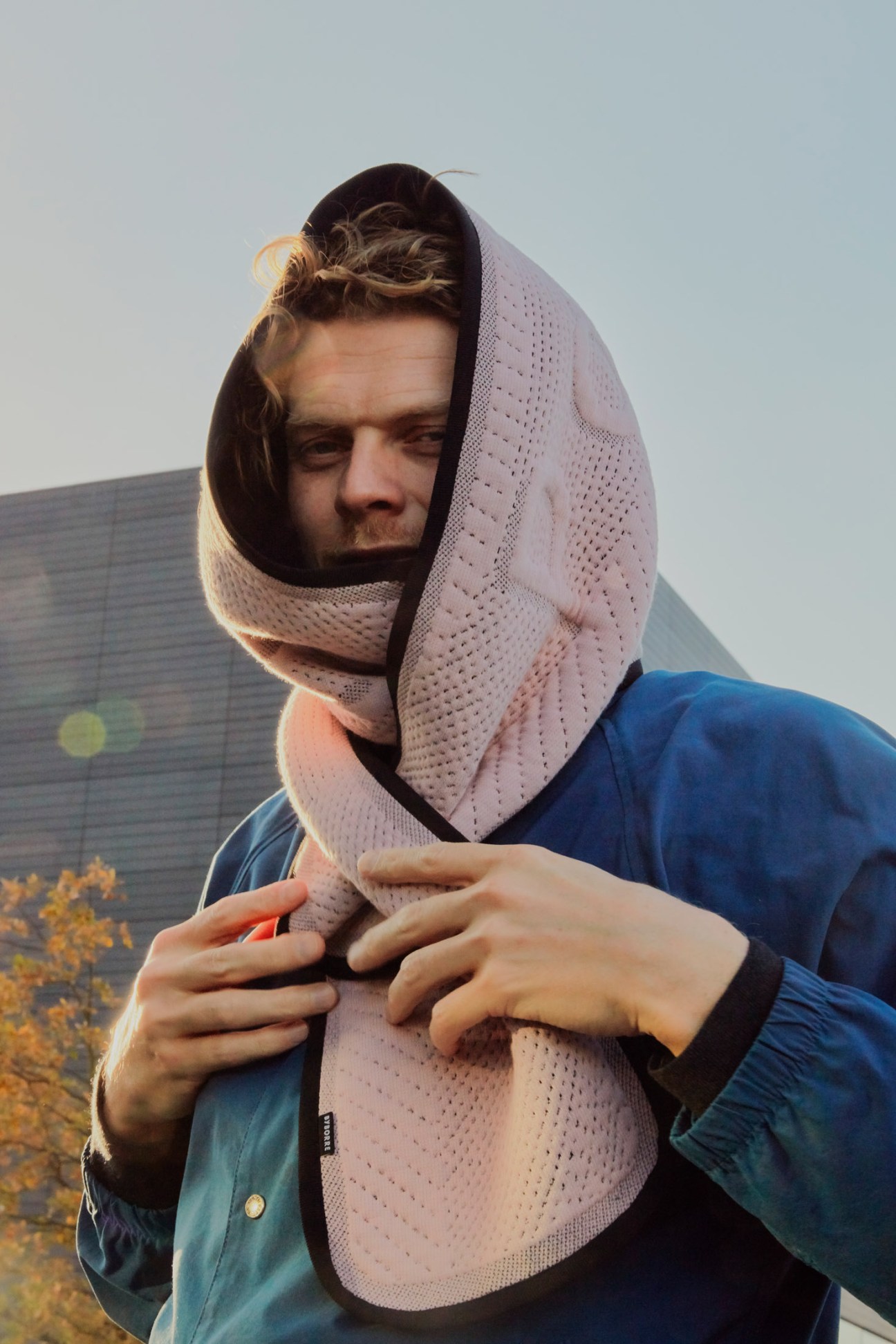 Man wearing pink knitted headwrap and blue jacket against urban background