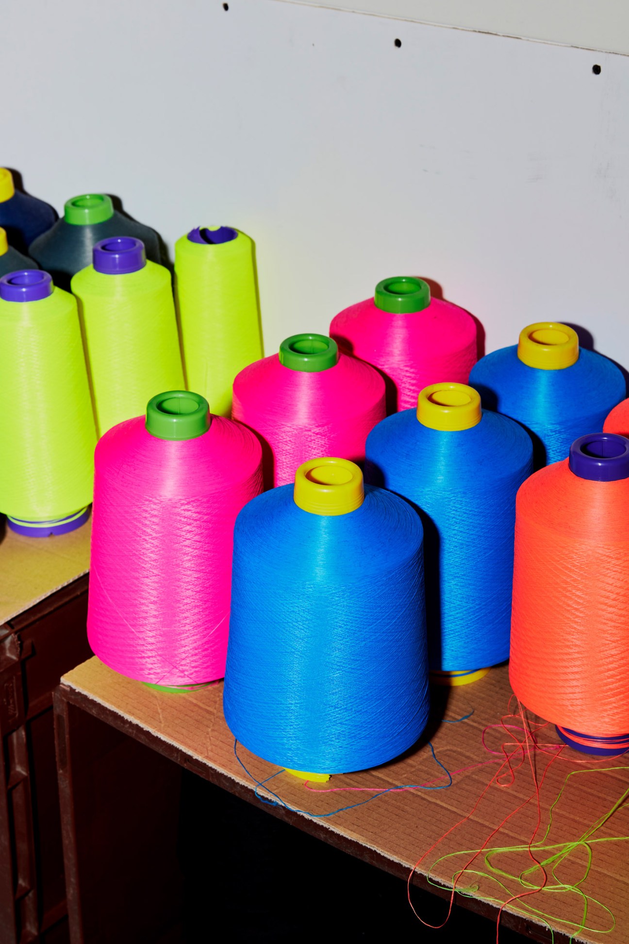 Colorful spools of thread in vibrant neon yellow, hot pink, blue, and orange arranged on a wooden table.