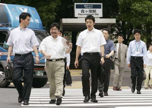 Japanese businessmen in white shirts and dark trousers crossing a street at a railway station during Cool Biz campaign.