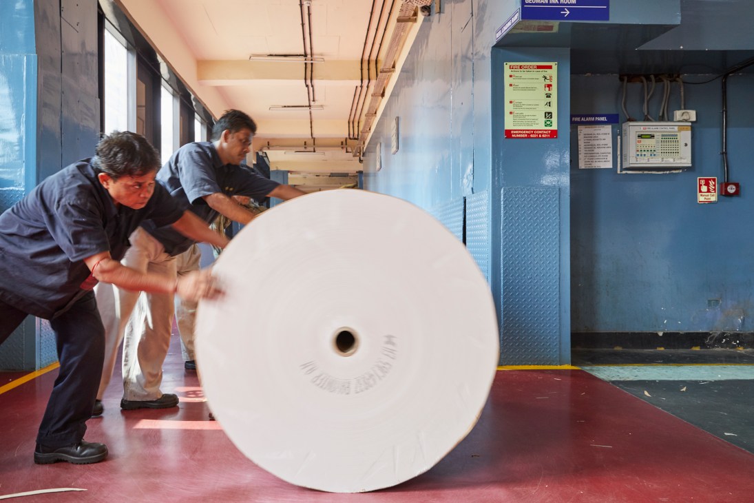 Workers handling a large white paper roll at Times of India's New Delhi printing press.