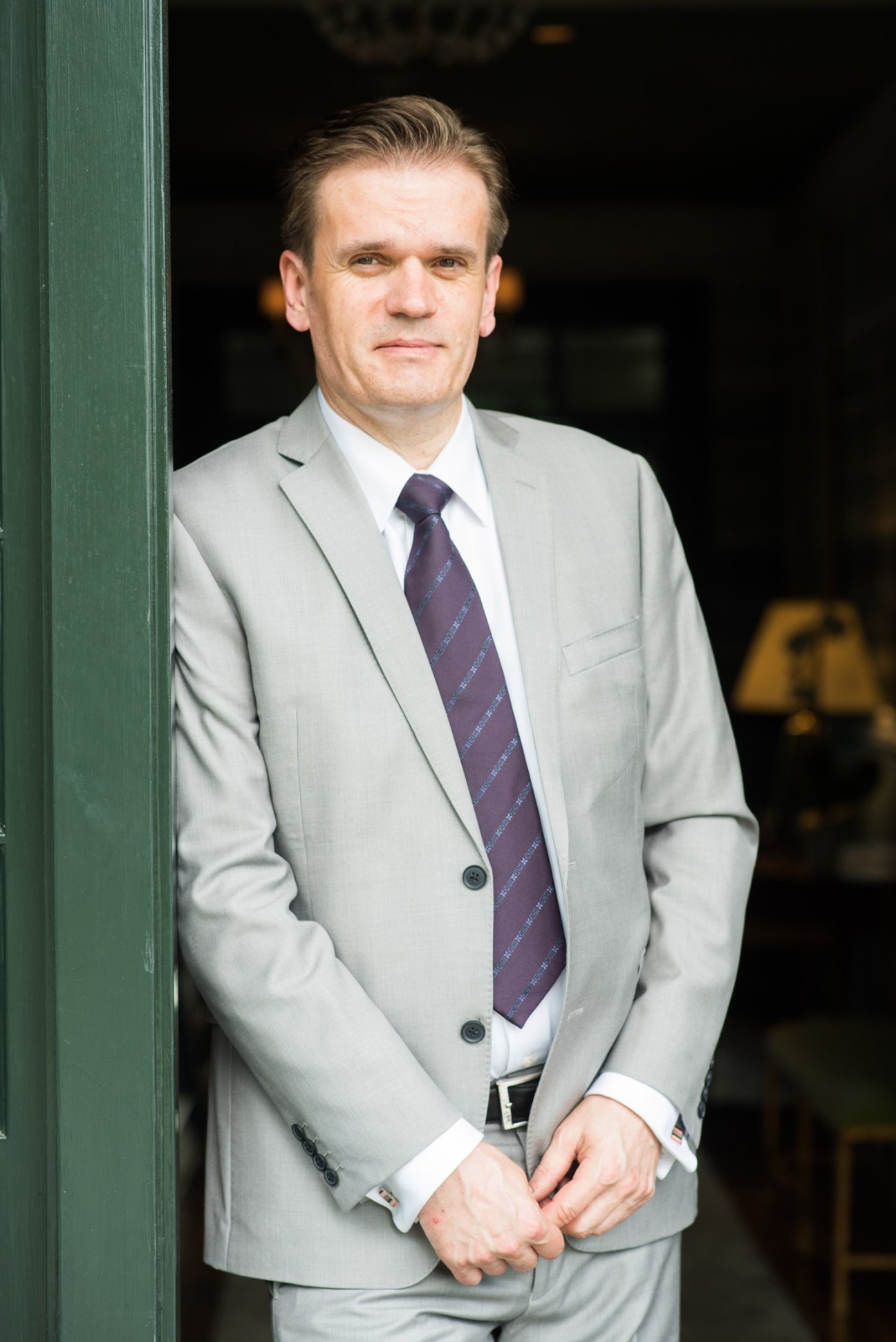 François Bladt, general manager of The Clifton hotel in Virginia, standing against a green doorframe wearing a light grey suit and dark tie.