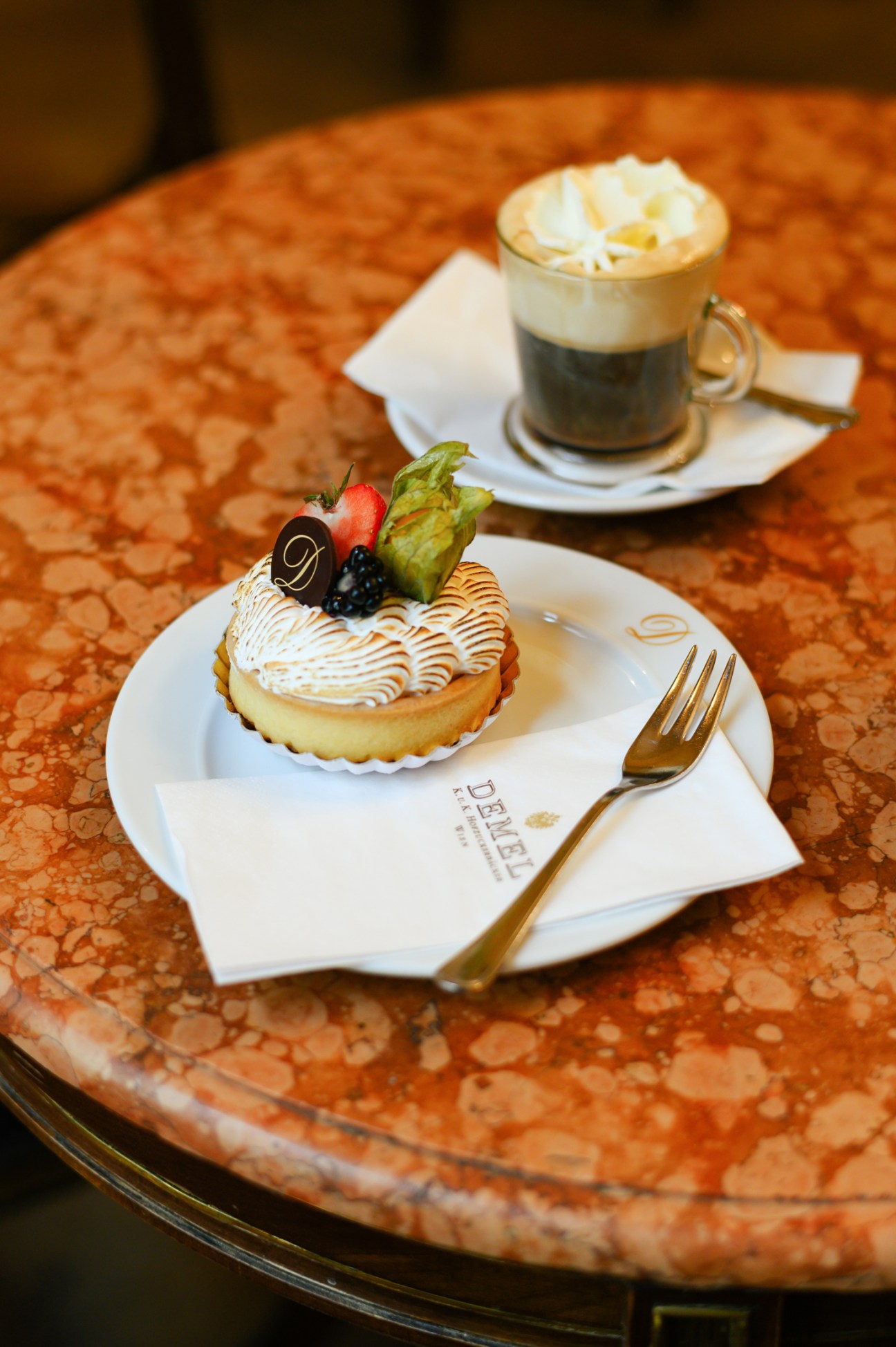 Lemon tart with meringue topping and berries on white plate with coffee cup at Demel cafe
