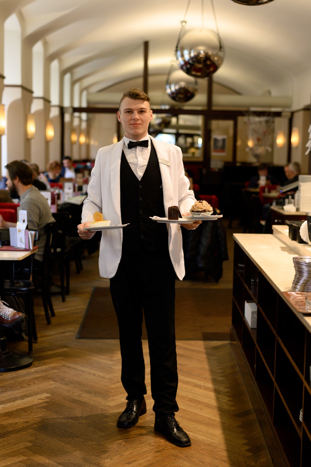 Waiter in formal attire carrying dessert plates in an elegant restaurant