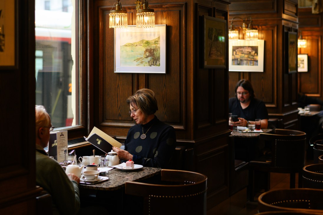 Woman reading menu at marble table in traditional Viennese café with wood paneling and chandeliers