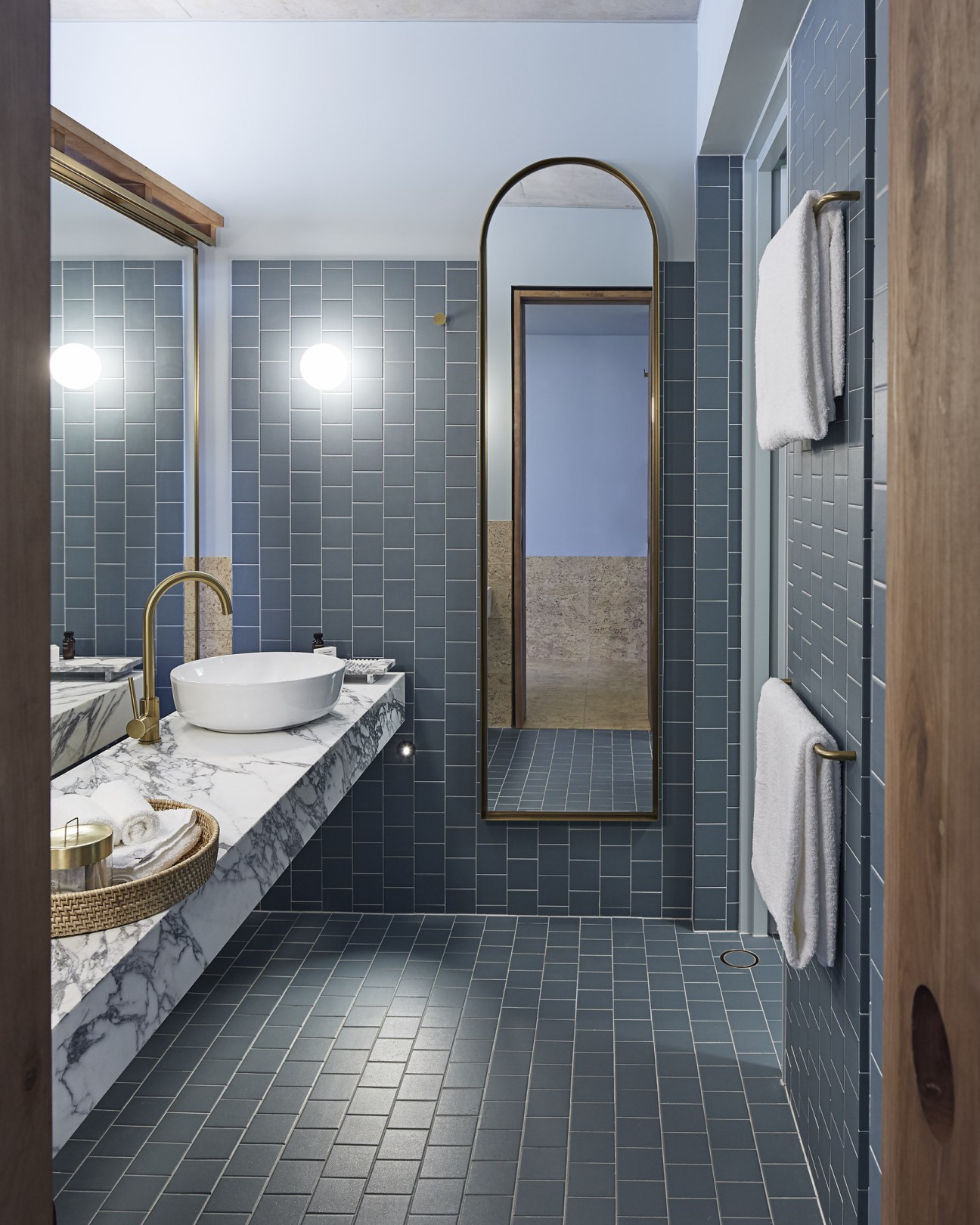 Modern bathroom with grey tile walls, marble vanity countertop, white vessel sink, and brushed brass fixtures and mirrors.