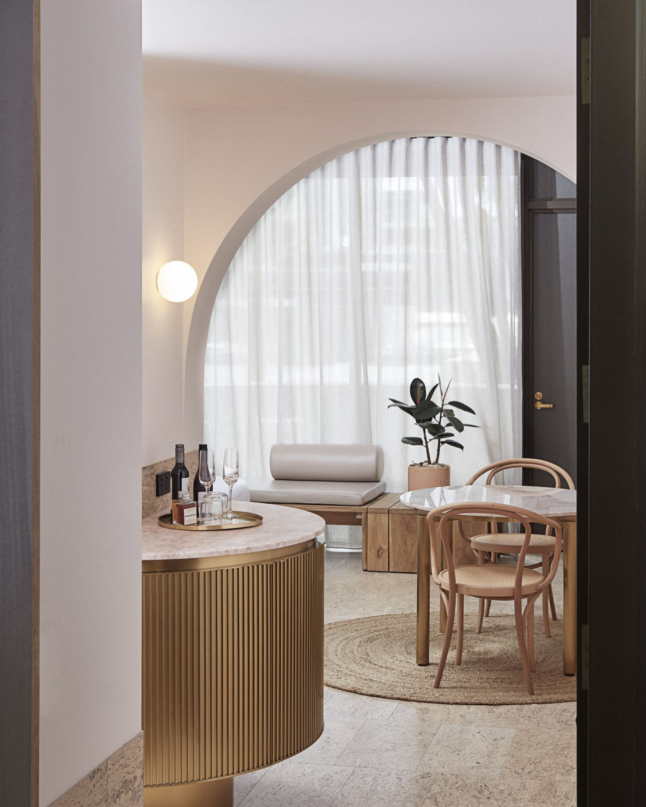 Modern hotel room interior with arched mirror, wooden furniture, potted plant, and marble surfaces.