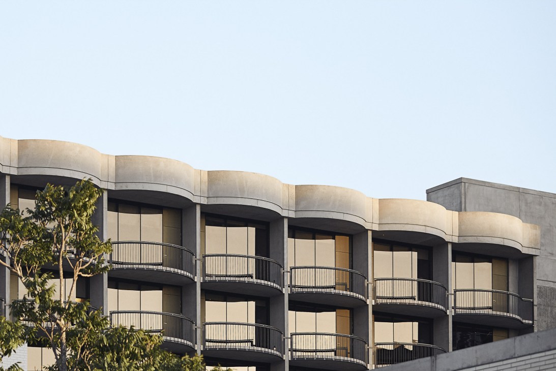 The Calile hotel exterior showing curved concrete and brick facade with curved balconies and palm trees against clear sky.