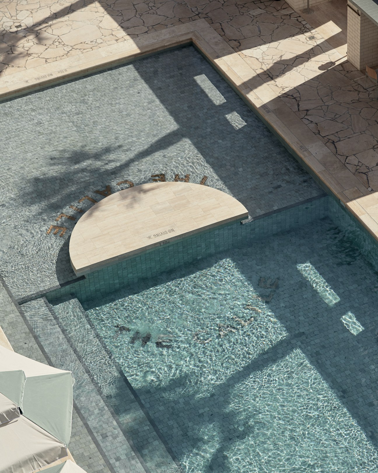 Overhead view of The Calile hotel's swimming pool with a white curved bench and green-tiled surround.