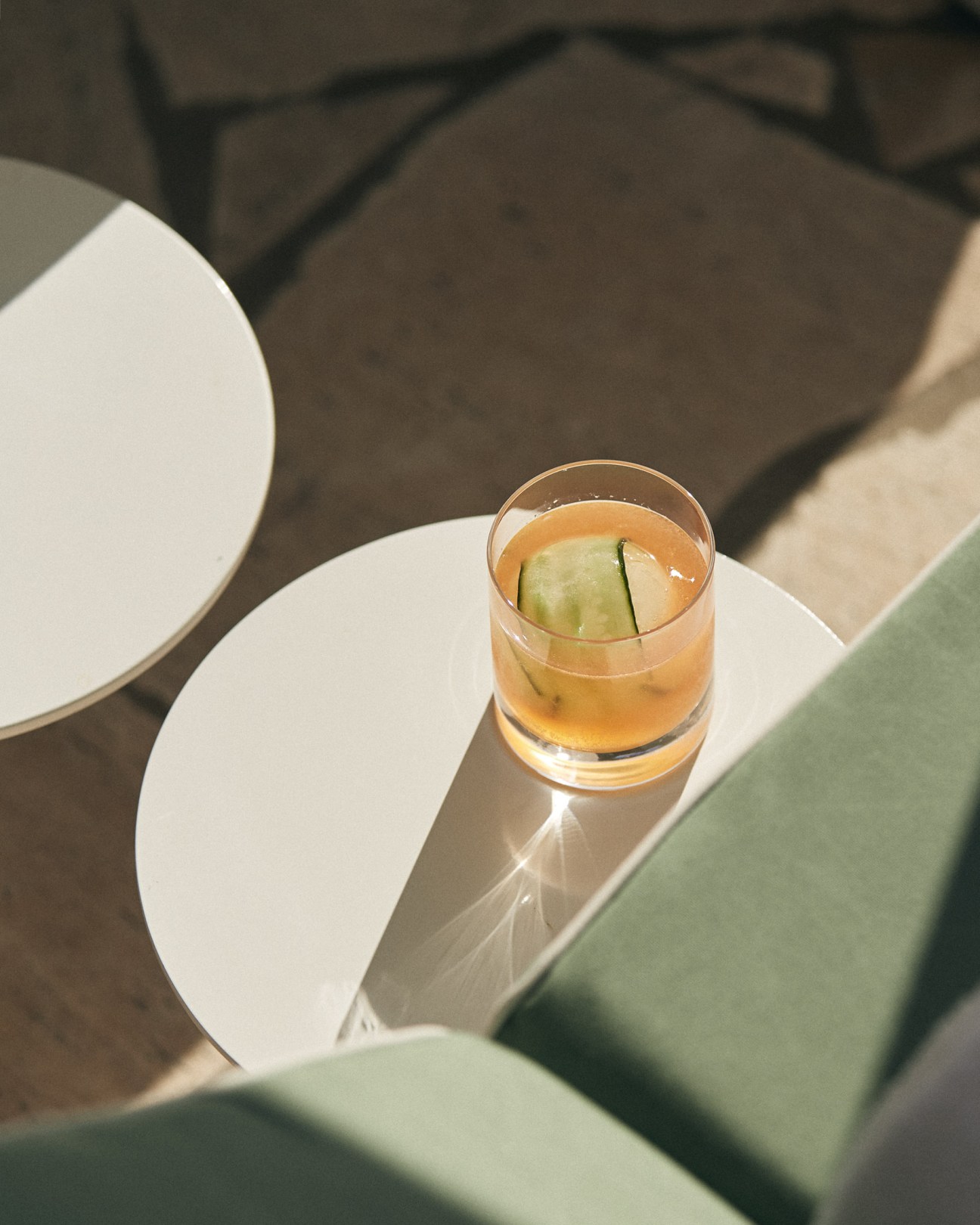 Overhead view of a cocktail with apple slice garnish on white plates in sunlight at The Calile hotel.