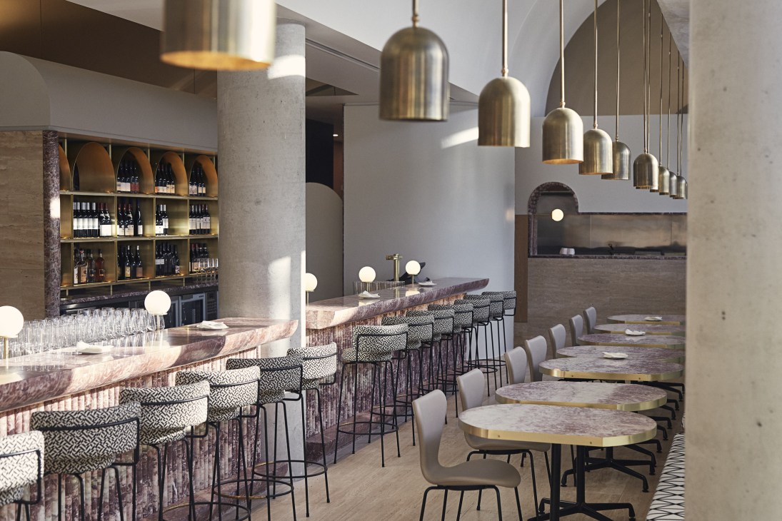The Calile hotel's lobby bar with brass pendant lights, marble countertops, and patterned bar stools.