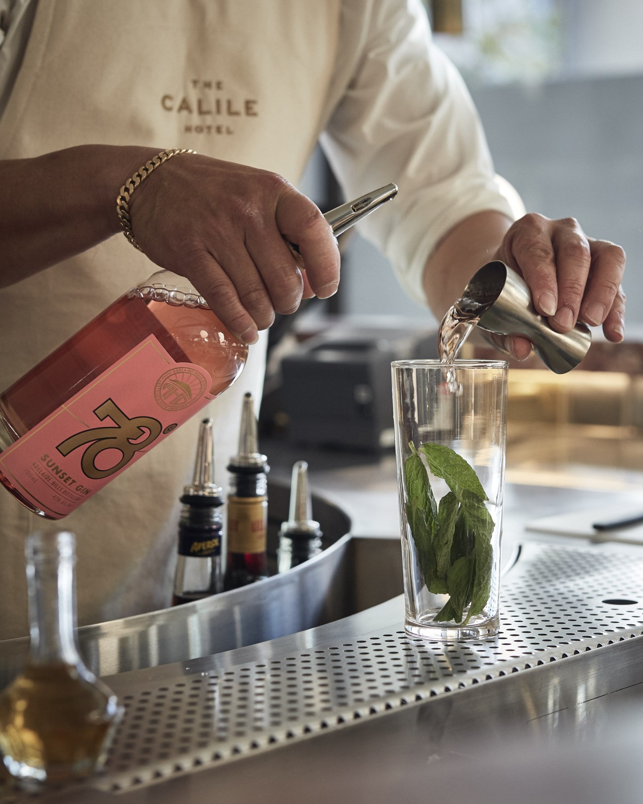Bartender at The Calile hotel pouring pink Sunset Gin into a glass with mint leaves.
