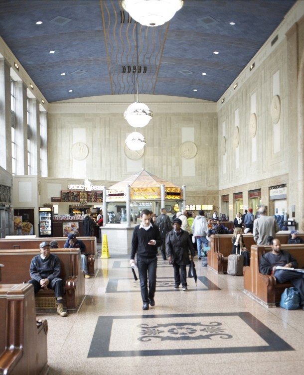 Interior of Newark's Penn Station showing ticket counters, pendant lighting, and passengers in the main hall.