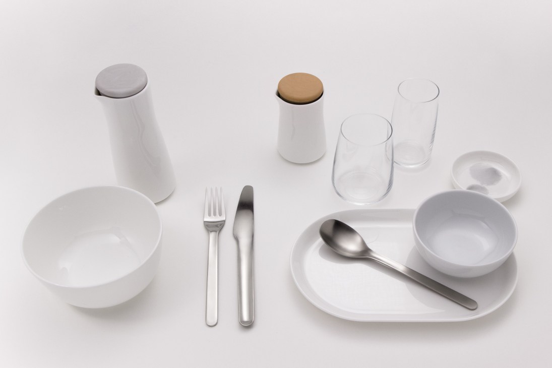 Minimalist white bone-china tableware set including plates, bowls, cups, glasses, salt and pepper shakers, and cutlery arranged on a neutral background.
