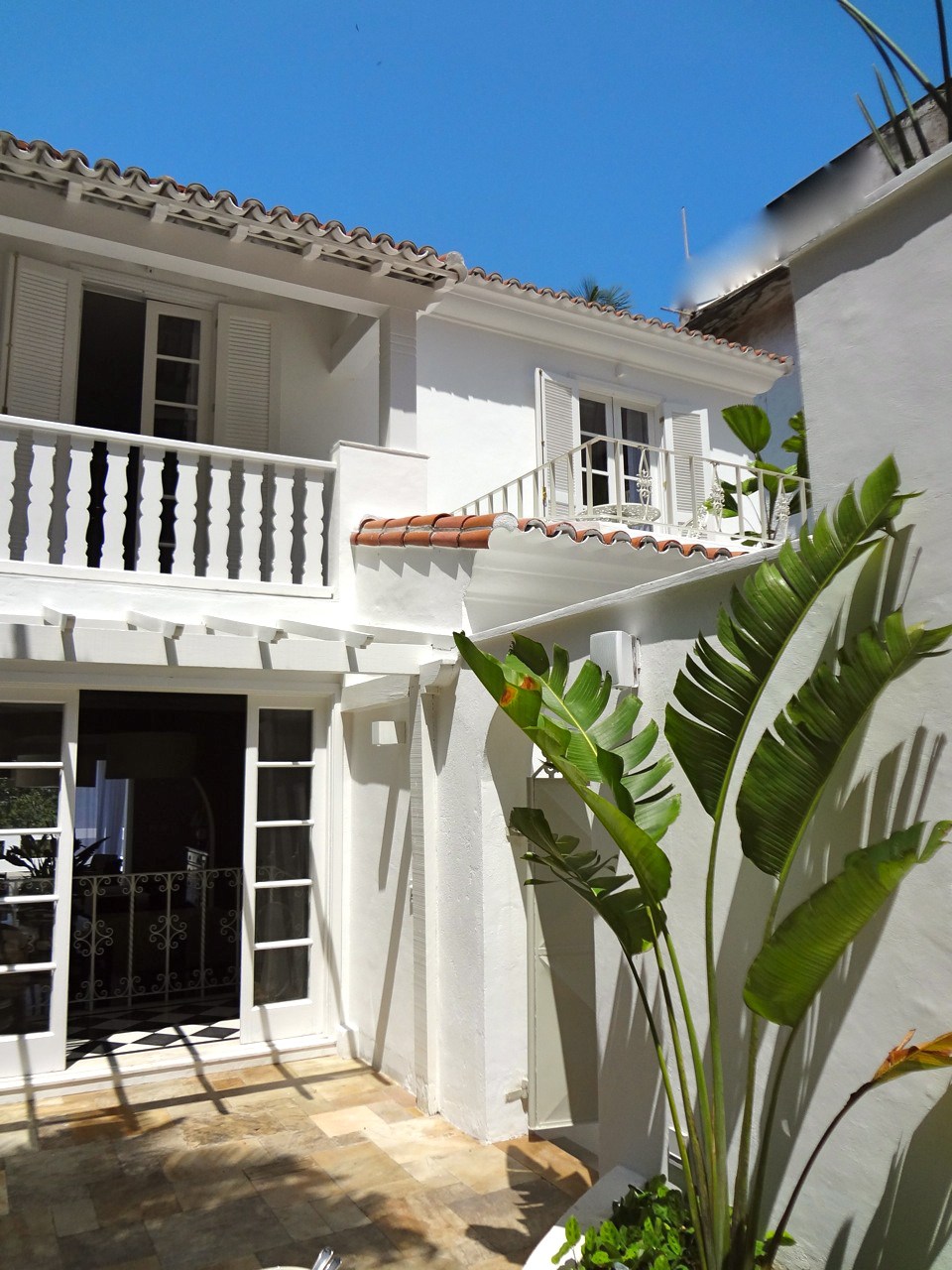 White colonial-style house with terracotta roof tiles, balconies and tropical plants in Rio de Janeiro.