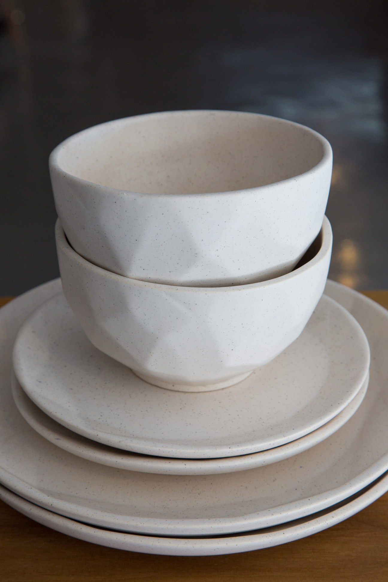 Stacked white handmade ceramic bowls and plates with speckled glaze.