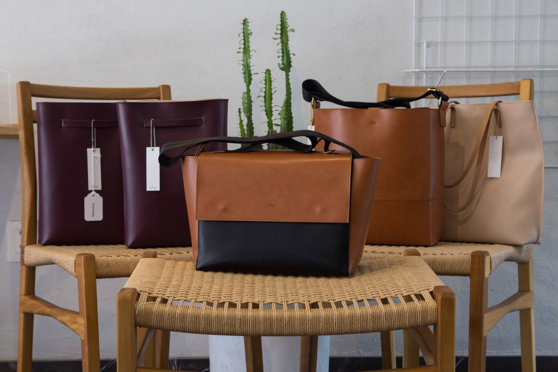 Ohja leather bags displayed on wooden chairs with cacti and sunglasses in a retail setting.