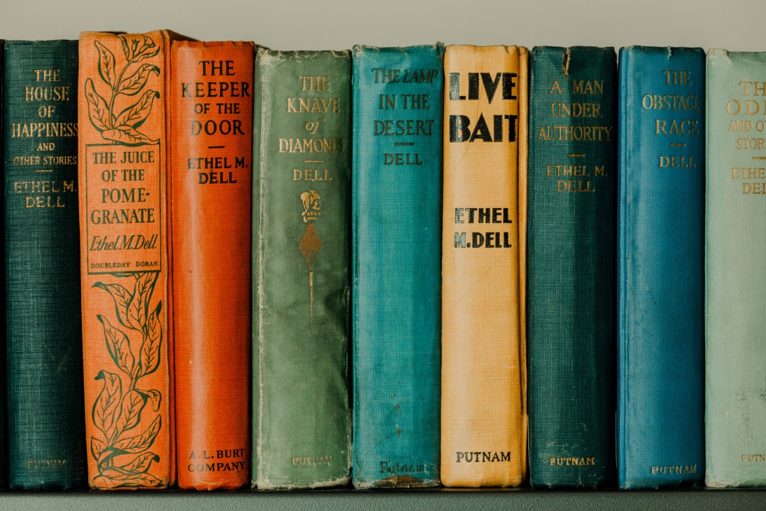 Vintage first edition books with colorful spines lined up, featuring works by Ethel M. Dell and other authors.