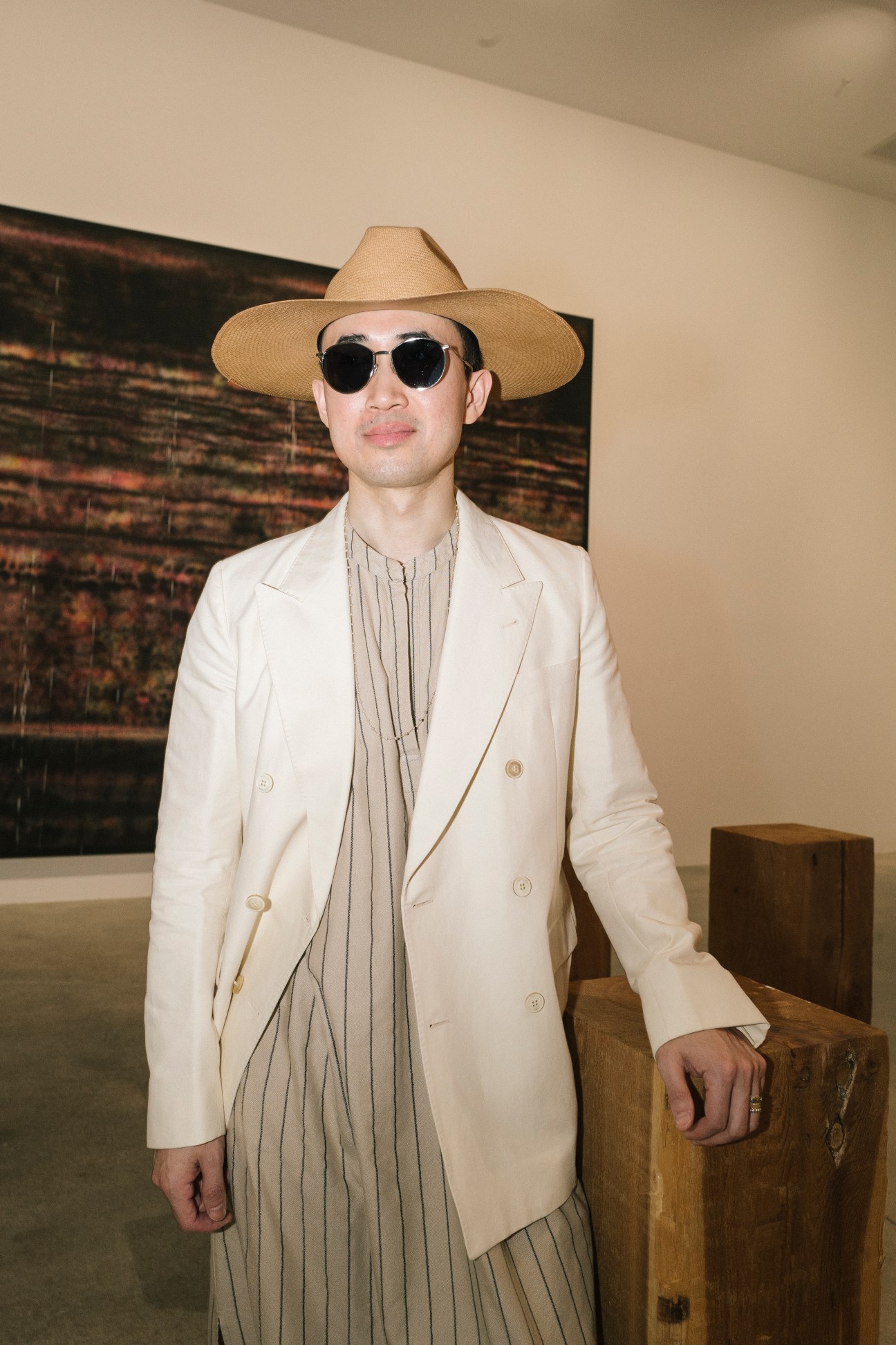 Man in beige suit jacket, striped shirt, straw hat and dark sunglasses at art gallery event