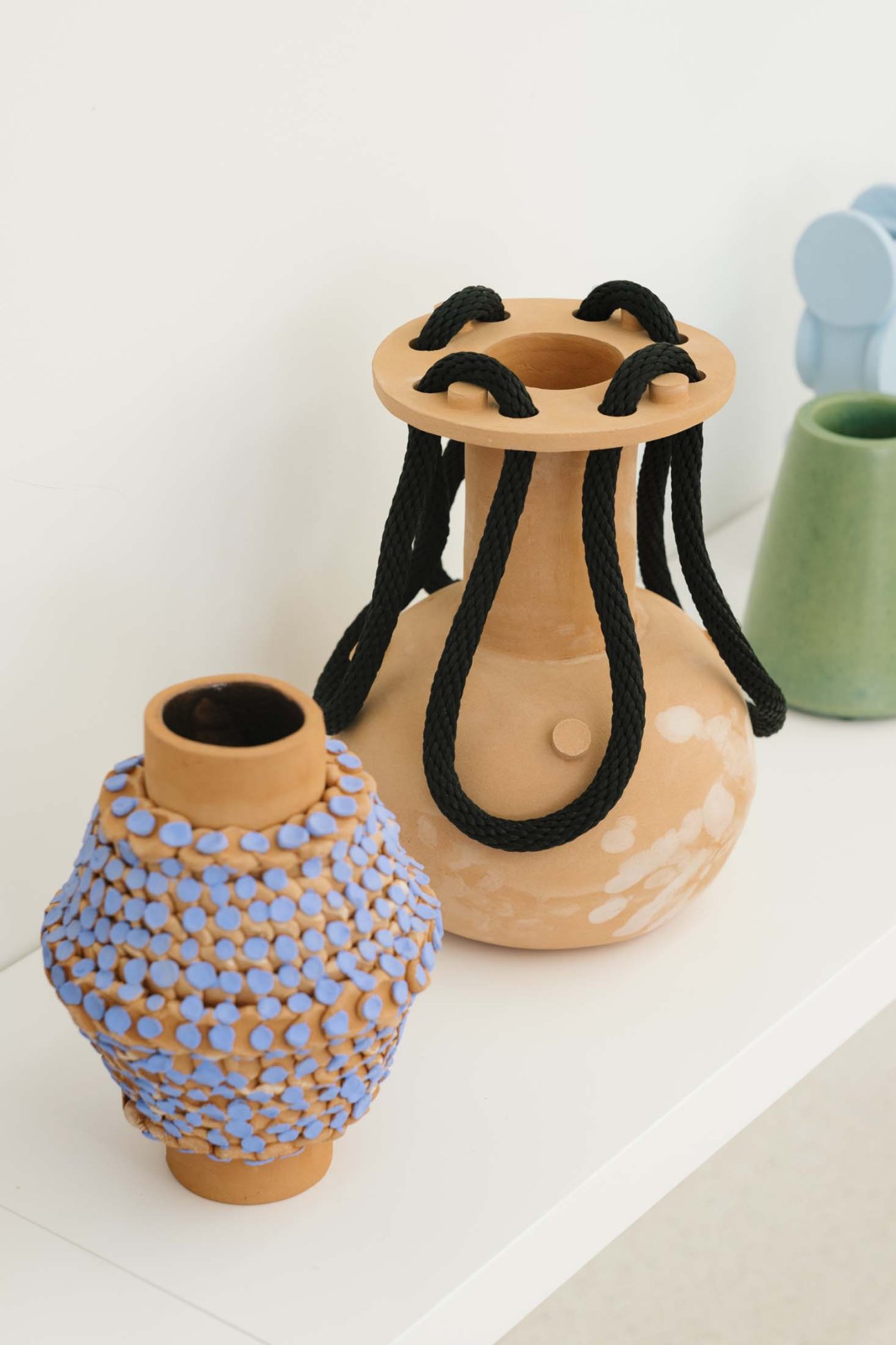 Ceramic vases with decorative details including blue polka dots and black rope handles displayed on white surface.