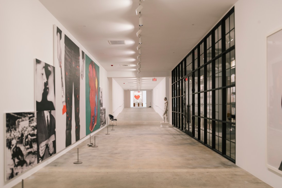 Long white museum corridor with artwork displayed on walls and floor-to-ceiling windows on one side