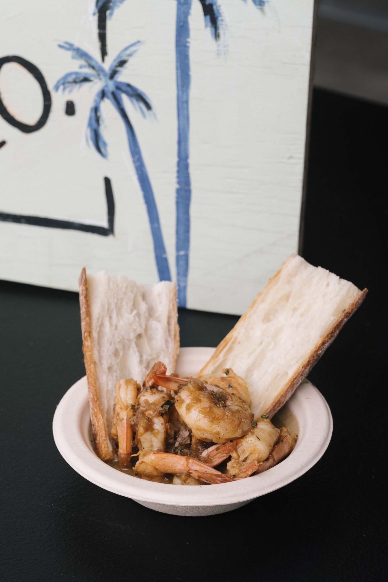 Shrimp dish with toasted bread on a white plate against a mural backdrop