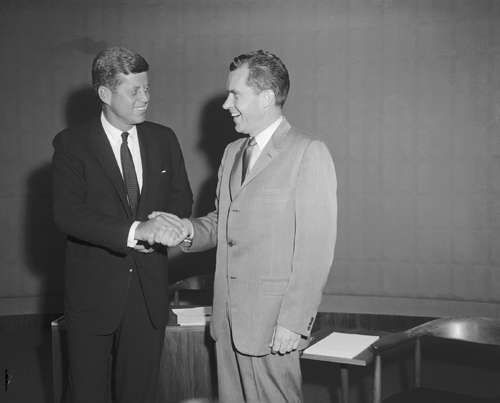 Two men in business suits shaking hands in black and white photograph.