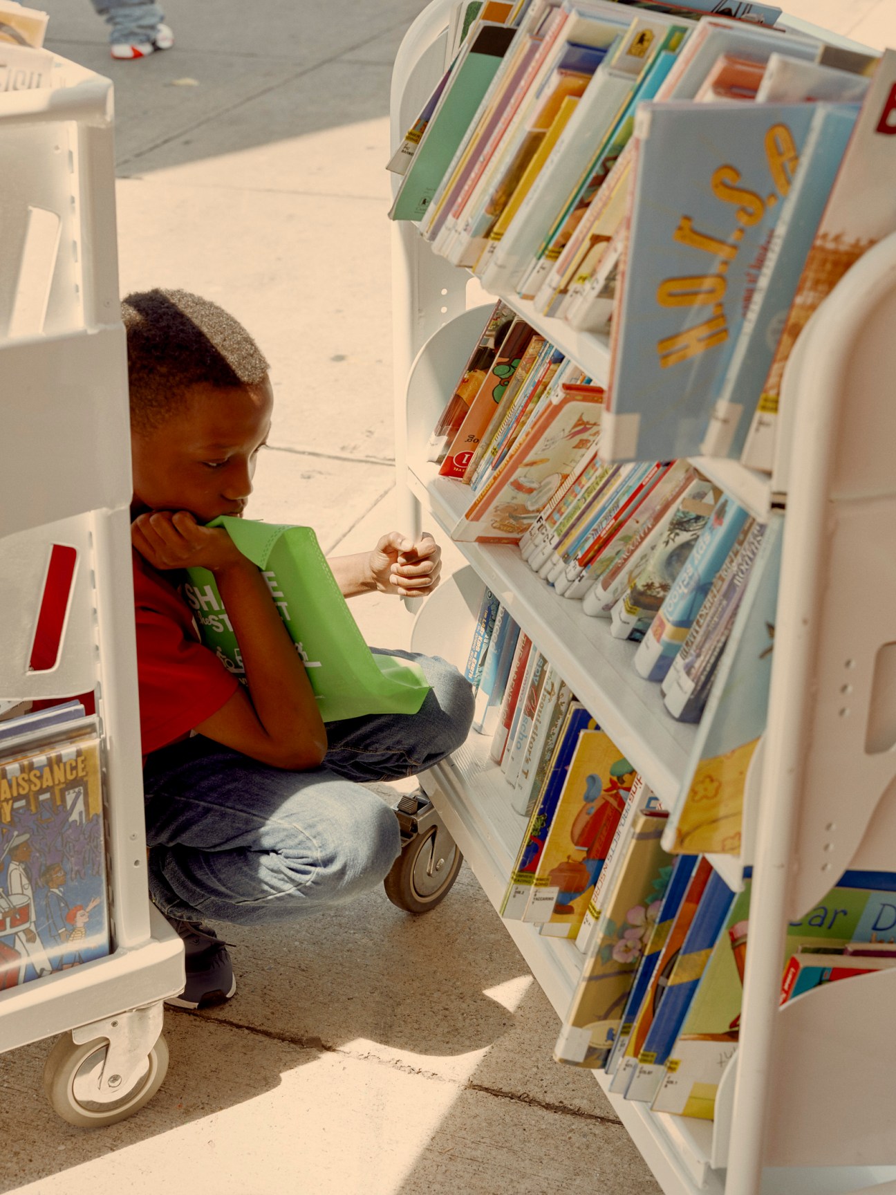 Young child browsing books on mobile shelving units set up on the street outside the NYPL Bookmobile.