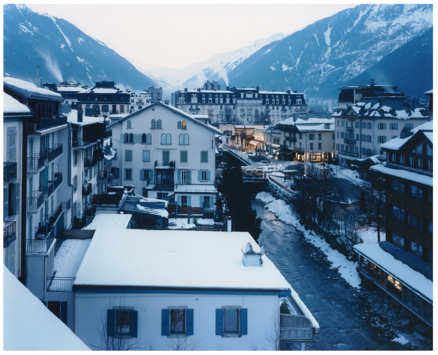 Snowy Chamonix town nestled in a narrow Alpine valley with snow-covered buildings and Mont Blanc visible in the distance.
