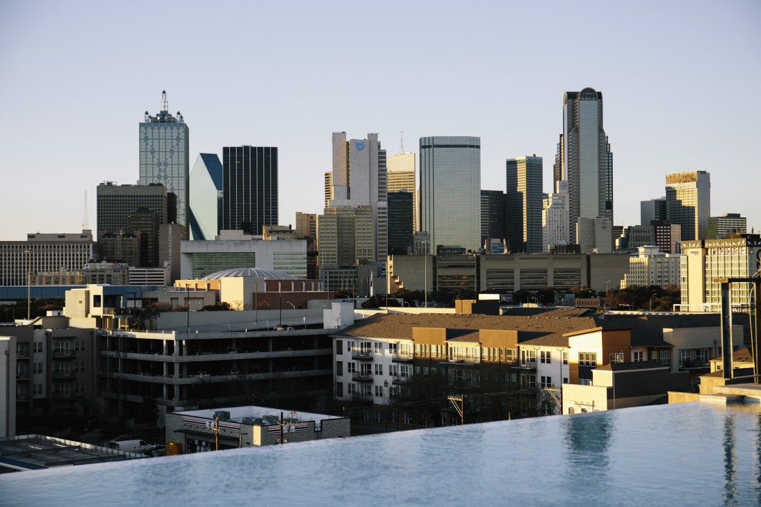 Dallas skyline at dusk with downtown high-rise buildings reflected in water below.