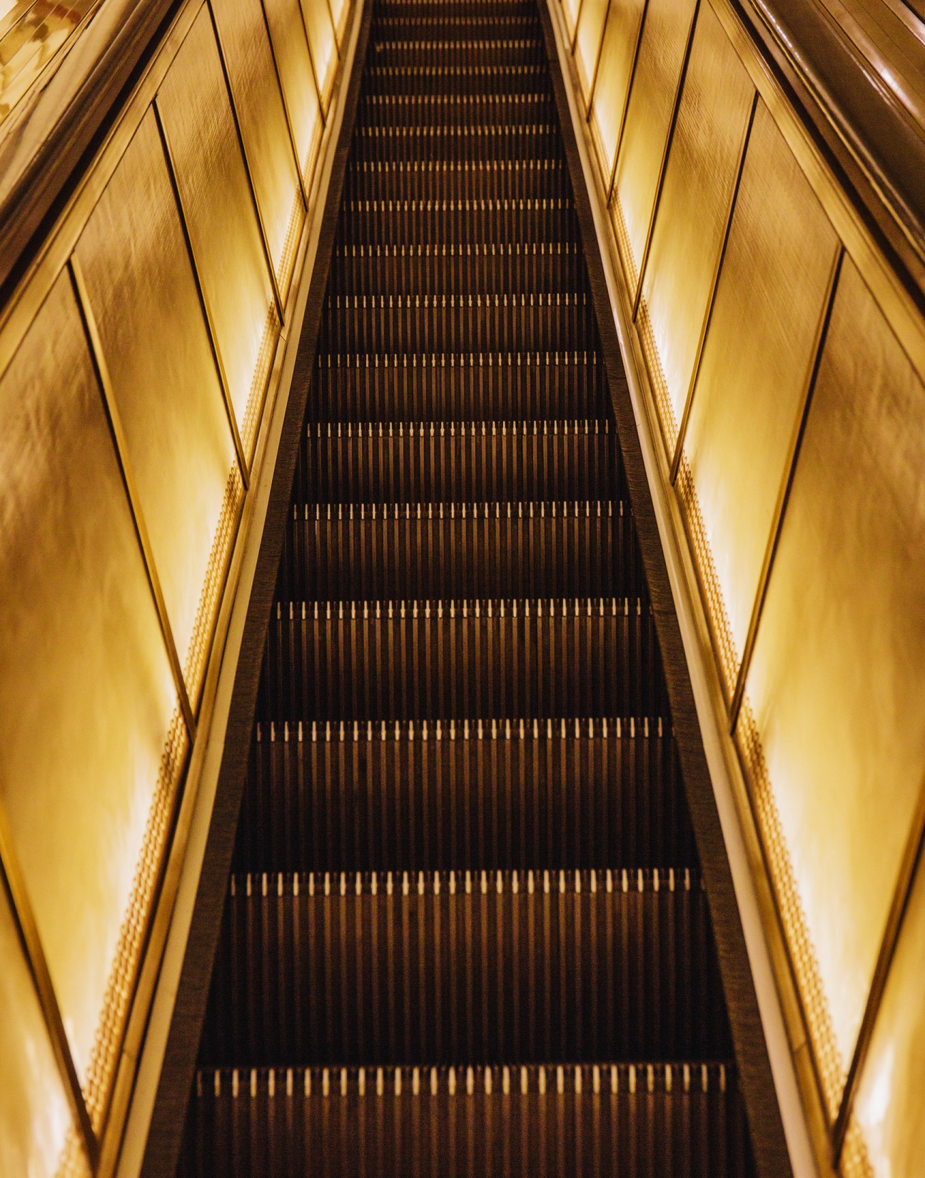 A gold escalator with illuminated sides stretches upward in a symmetrical composition at Neiman Marcus.
