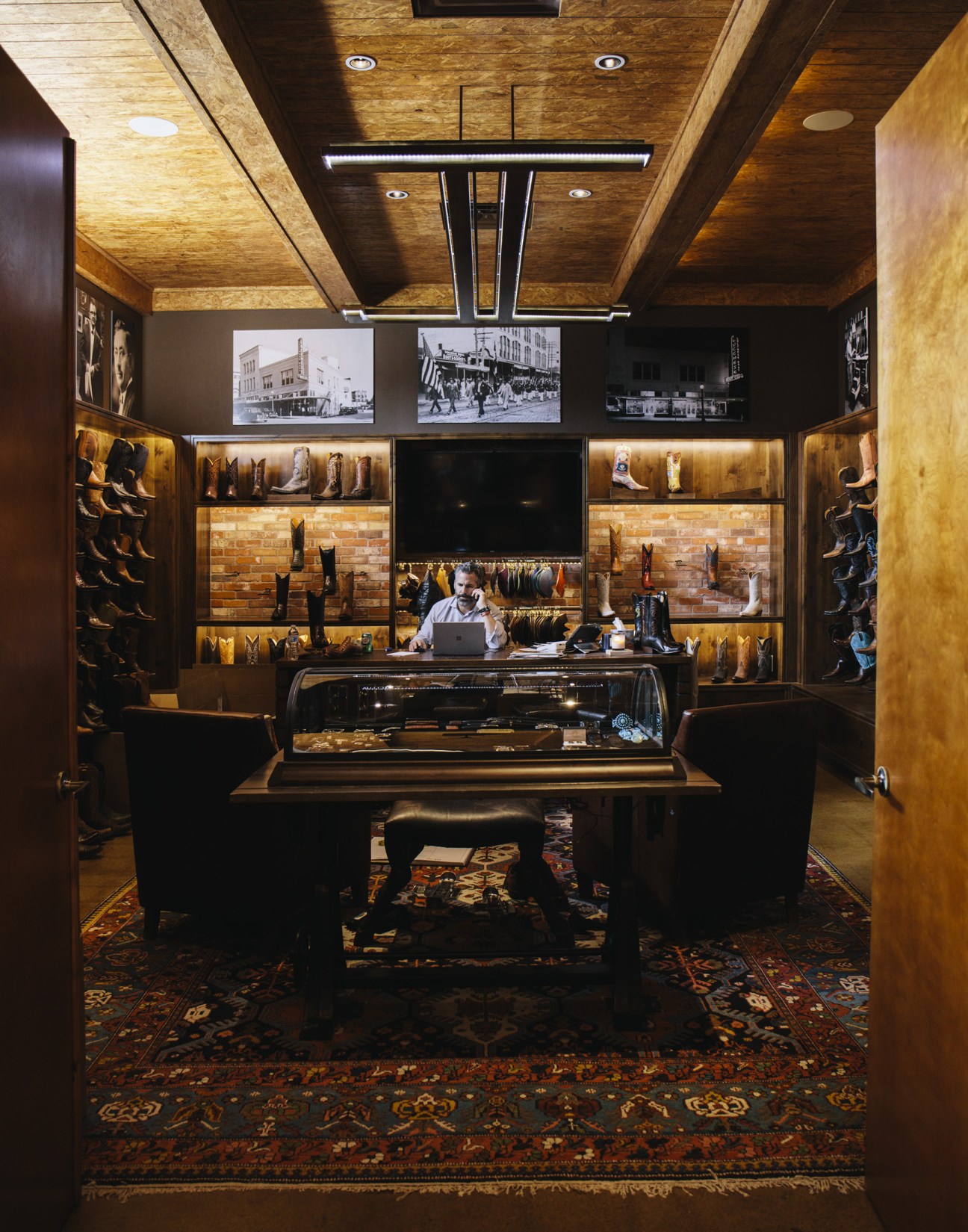 Interior of Lucchese leather boot store with illuminated display cases and historical photographs on walls.