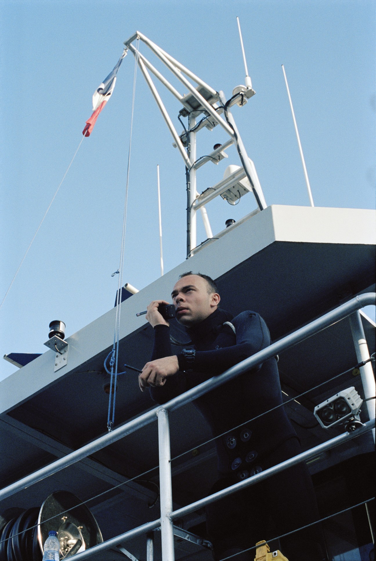 Sailor in navy uniform on ship deck surveying training operation under clear sky.