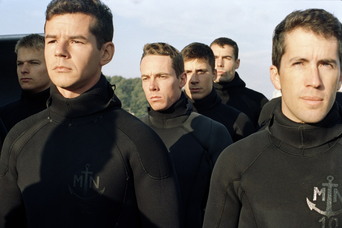 French naval officers in black wetsuits with Marine Nationale insignia stand on deck.