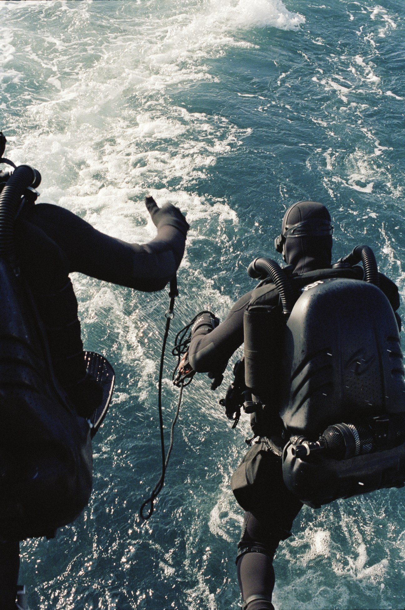 French naval divers in full diving gear preparing to enter choppy Mediterranean waters from a boat.