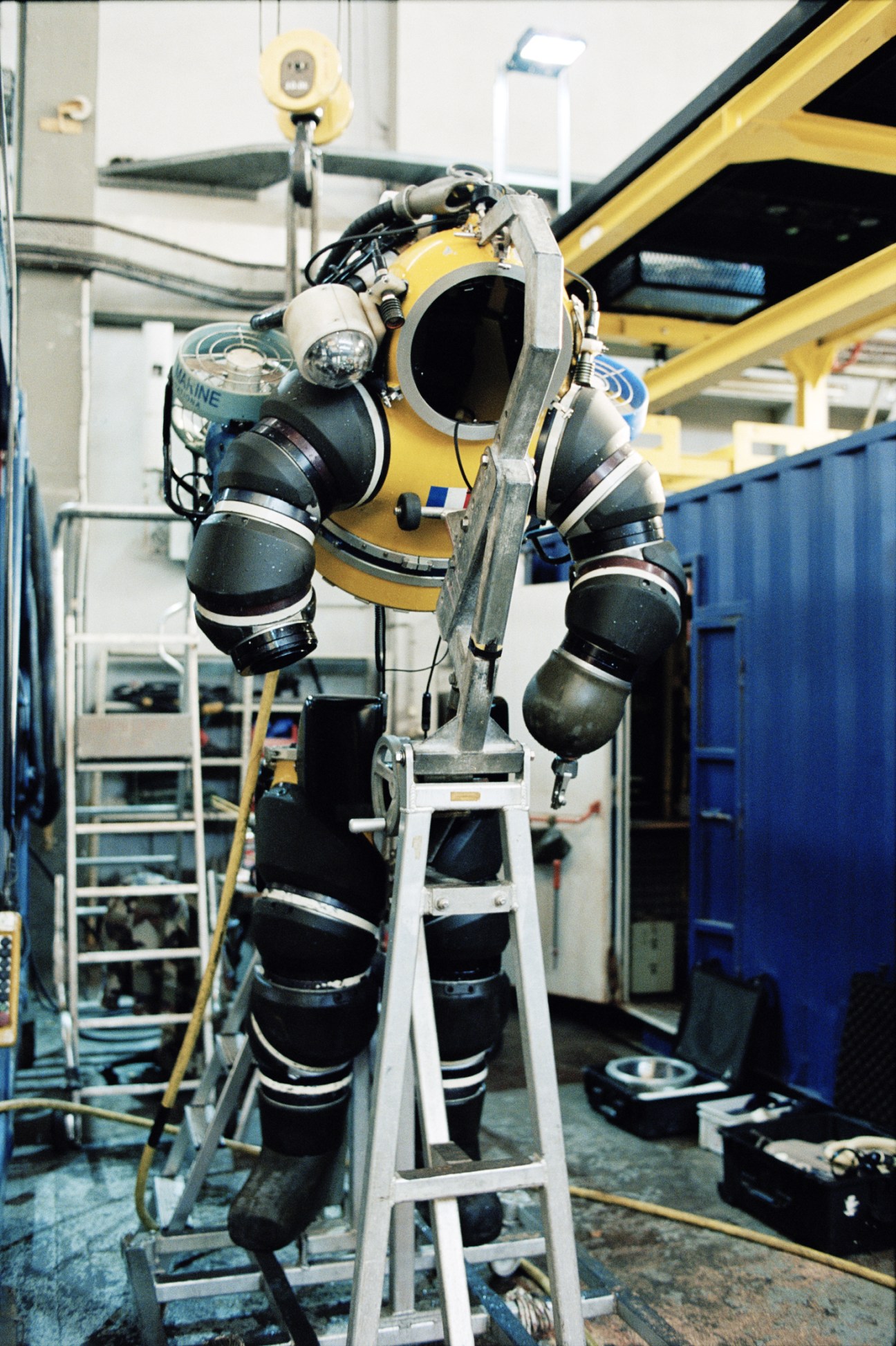 Yellow and black Newtsuit deep-sea diving suit suspended on a stand in a hangar.