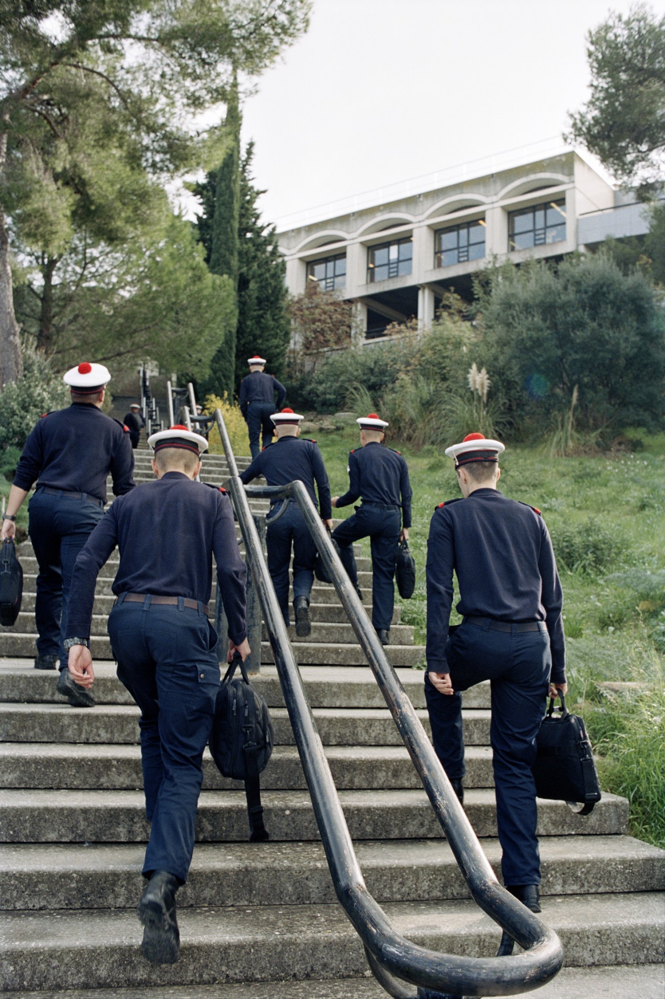 French sailors in navy uniforms with red-trimmed caps climbing stairs while carrying a rope.