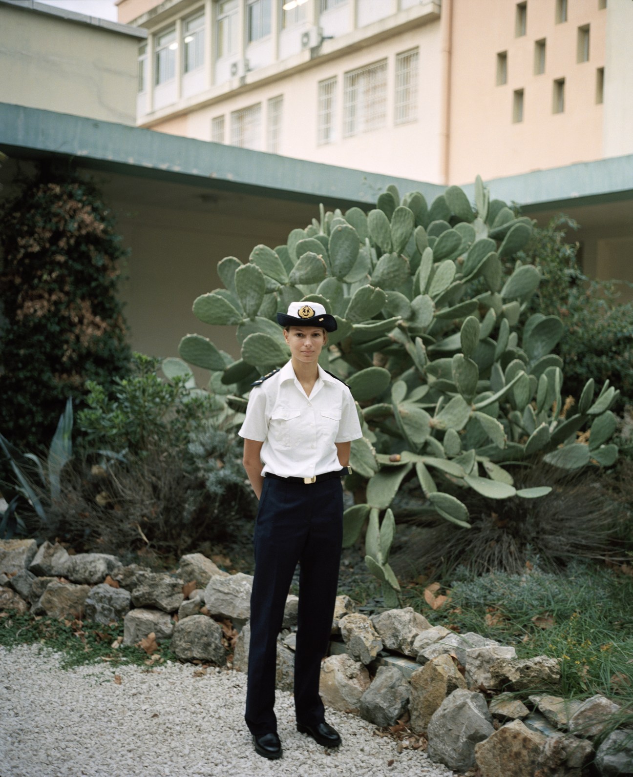 Young French naval recruit in white shirt and cap standing in courtyard with cacti